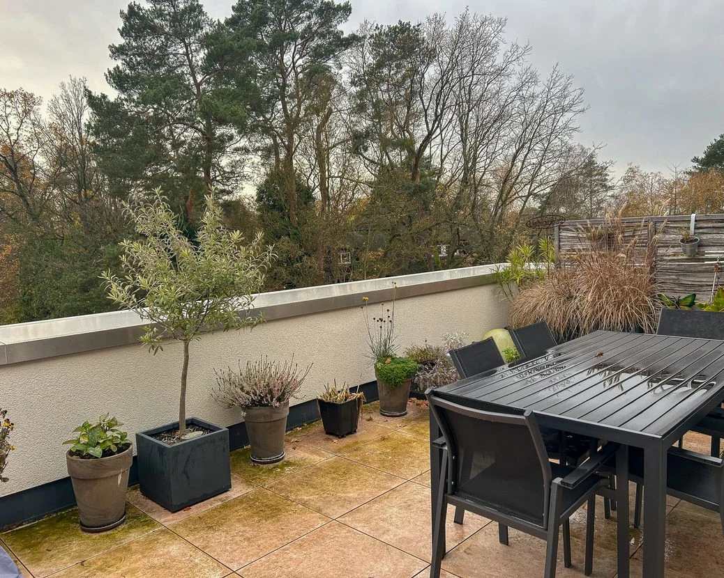 Originalfoto einer Dachterrasse mit Pflanzenkübeln und dunklem Gartentisch